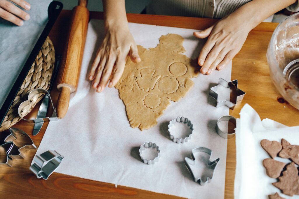 Hands rolling and cutting dough for homemade cookies with baking tools on a wooden table.